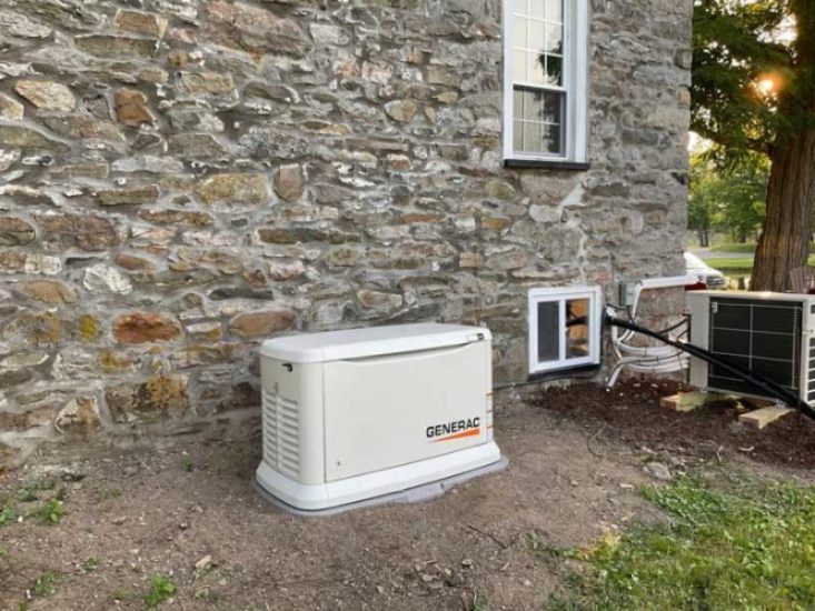 A Generac generator placed in a garden beside a house's wall at Blairstown, NJ