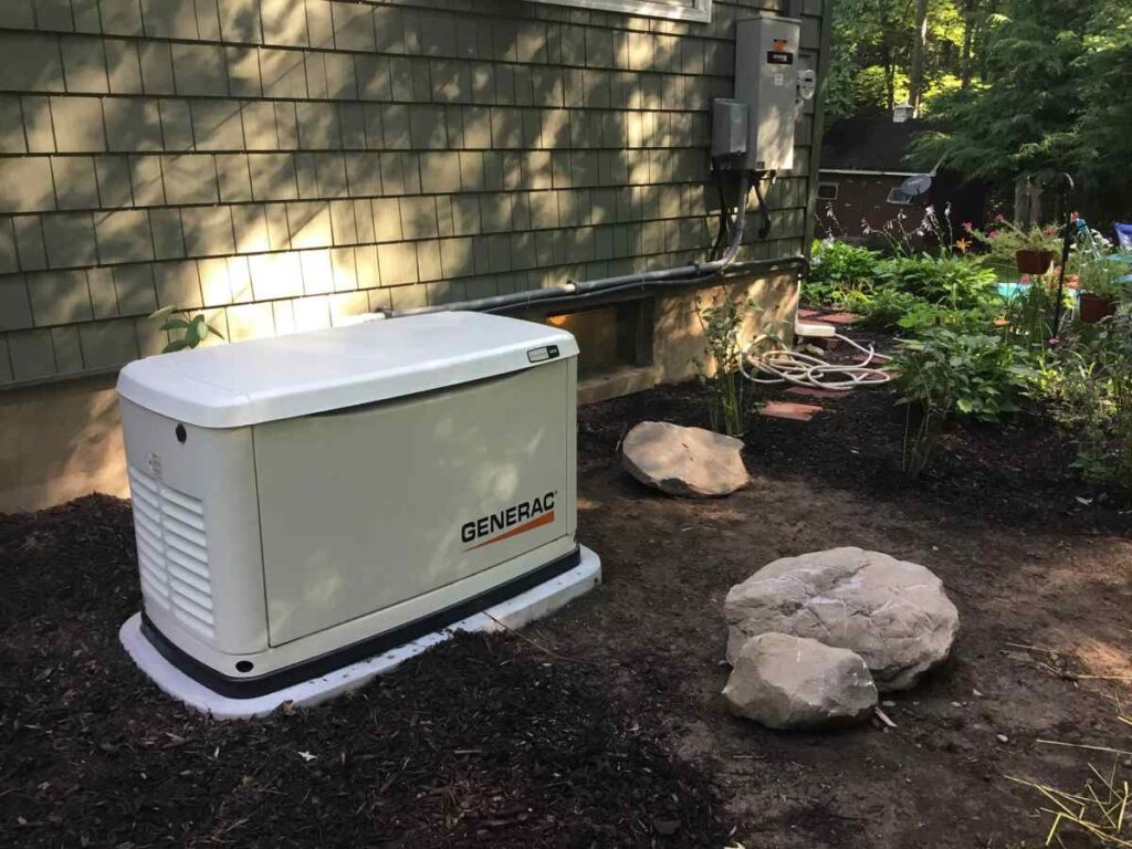 Generac standby generator installed by Seidel Electric outside a residential home near the electrical panel surrounded by plants and rocks