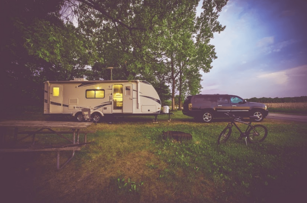 A four door black SUV pulling an RV in a wooded area