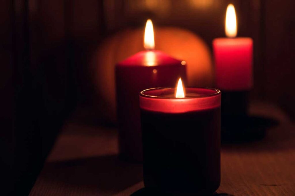 Three red candles sitting in front of a pumpkin 